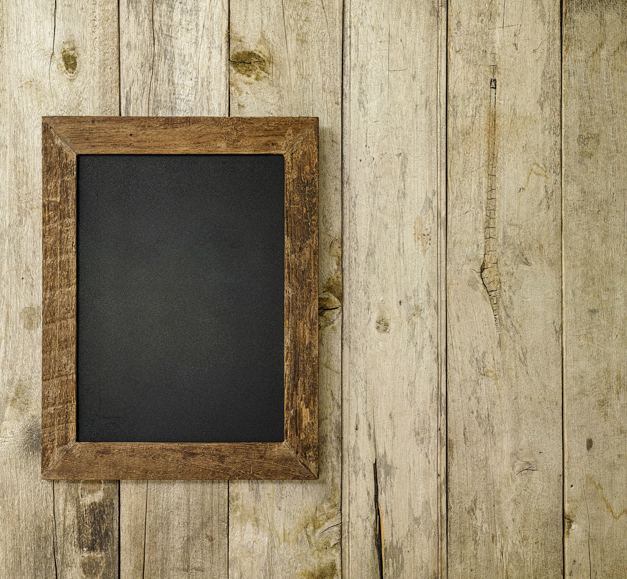 An old wooden framed blackboard on an old weathered wooden plank wall background.